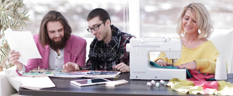 Empresaria sonriente del sastre que se sienta en la m?quina de coser y la fabricaci?n de la ropa hecha a mano mientras que comerc imagen de archivo libre de regalías Empresaria sonriente del sastre que se sienta en la m?quina de coser y la fabricaci?n de la ropa hecha a mano mientras que comerc imagen de archivo libre de regalías