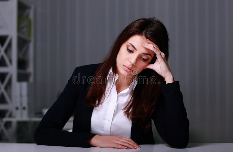 Empresaria triste joven que se sienta en la tabla en su lugar de trabajo foto de archivo libre de regalías Empresaria triste joven que se sienta en la tabla en su lugar de trabajo foto de archivo libre de regalías