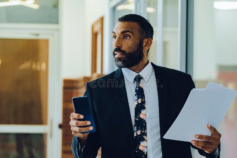 Empresario adulto medio barbudo hombre negro hombre de negocios vestido con traje portando papeles y smartphone caminando en el ca imágenes de archivo libres de regalías
