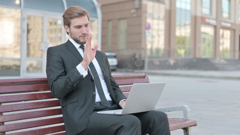 Empresario hablando en video llamada mientras se sienta al aire libre en el banco foto de archivo libre de regalías