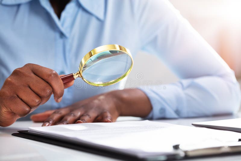 Close-up Of A Businessperson`s Hand Looking At Contract Form Through Magnifying Glass. Close-up Of A Businessperson`s Hand Looking At Contract Form Through Magnifying Glass