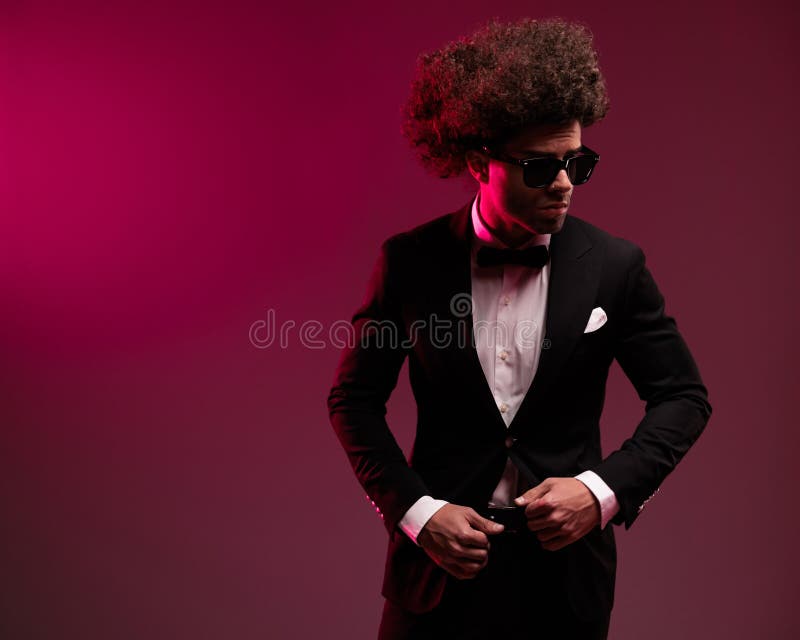 Empresario sexy con pelo rizado mirando hacia un lado y arreglando el esmoquin foto de archivo libre de regalías