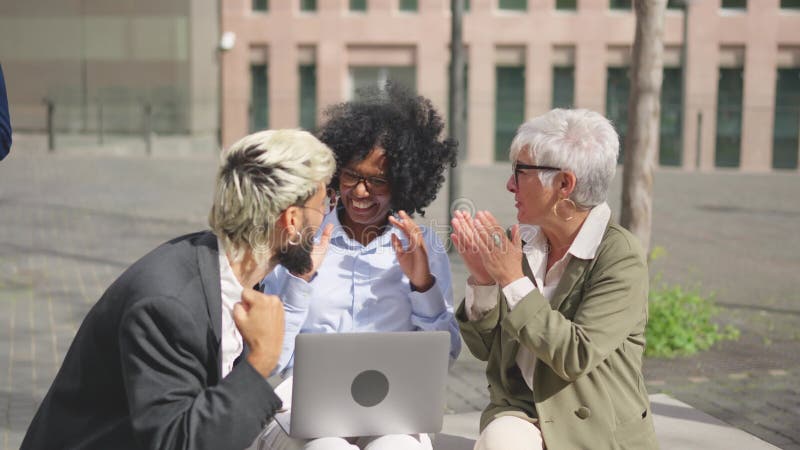 Empresarios levantando puño para celebrar las noticias usando una laptop al aire libre