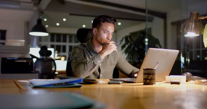 Empresário biracial focado na mesa usando laptop no escritório em câmera lenta noturna