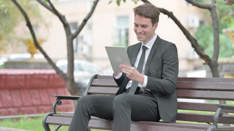 Empresário comemorando em tablet enquanto sentado no banco