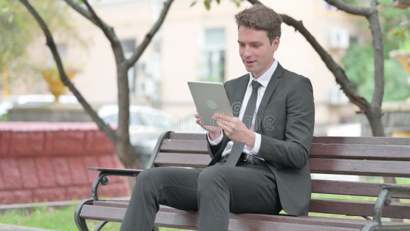 Empresário conversando em vídeo sobre tablet enquanto se senta no banco