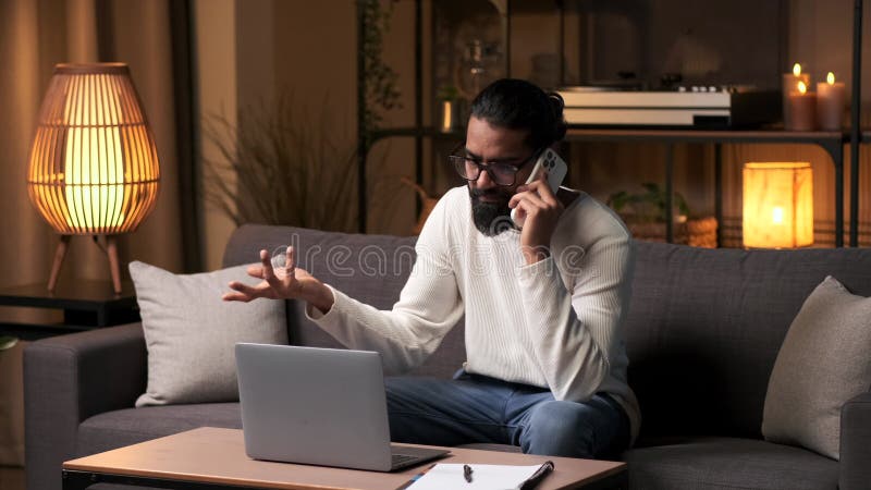 Empresário distraído falando ao telefone e trabalhando no laptop à noite