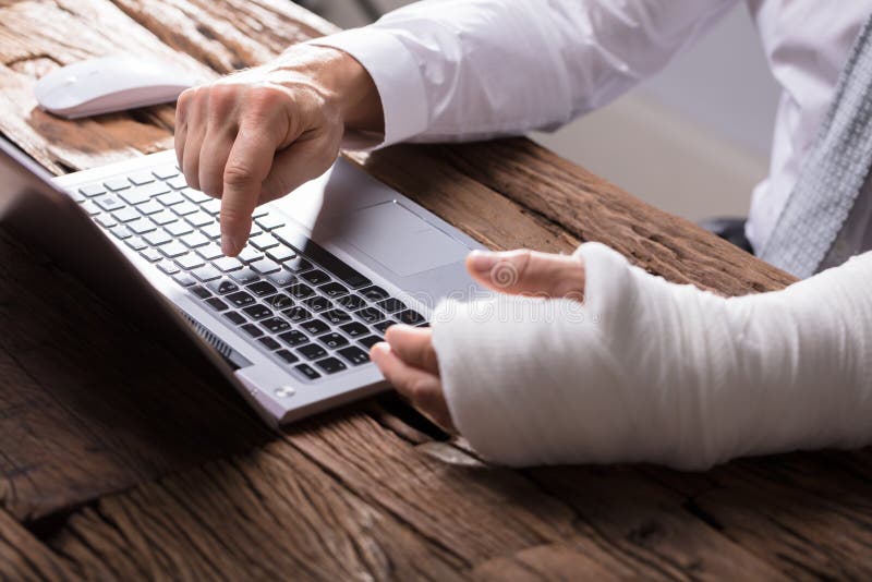 Empresário With Hand Injury que usa o portátil foto de stock Empresário With Hand Injury que usa o portátil foto de stock