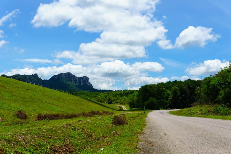 empty asphalt country road along the wall of dam with green grass and blue sky with clouds and mountain background in countryside.