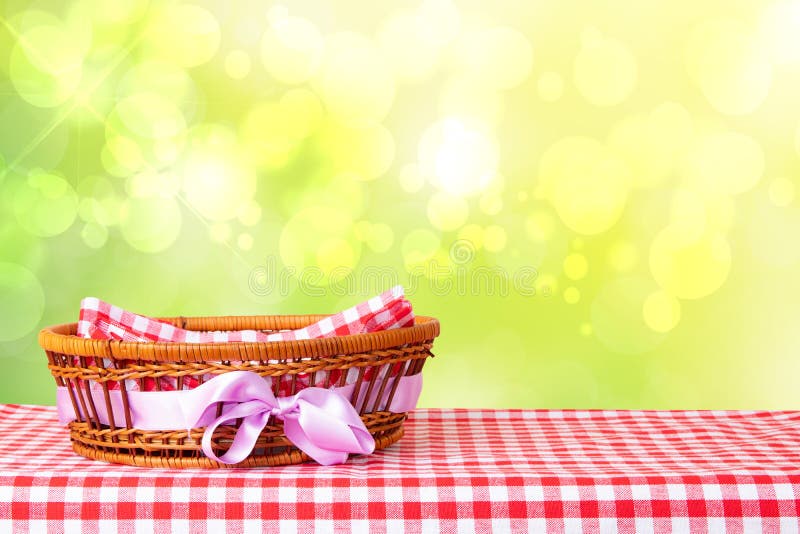 Empty basket with purple ribbon on red checkered tablecloth with abstract bright yellow spring or summer background. For your food and product display montage.