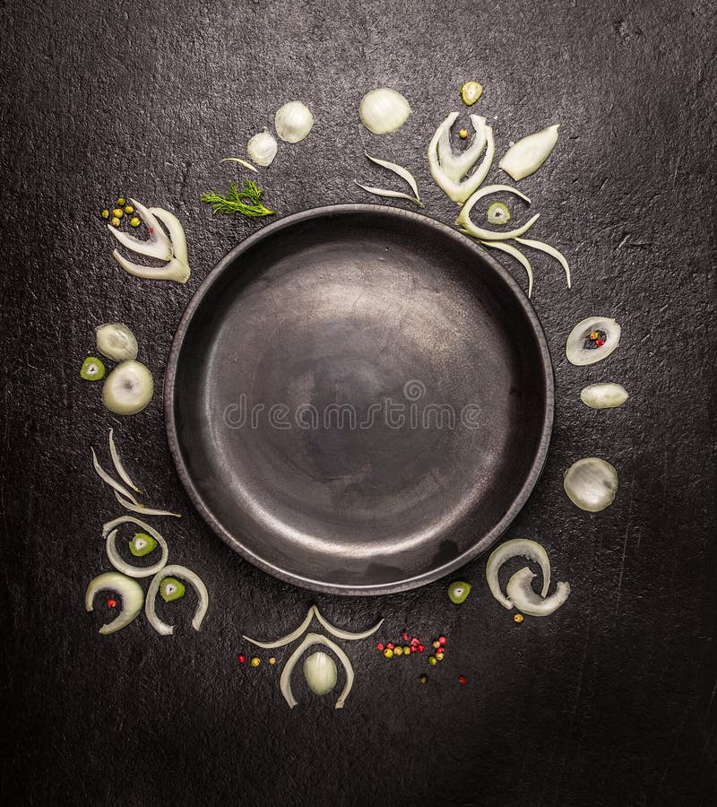 Empty black plate with frame of onion slices and spices on dark stone background, top view stock images