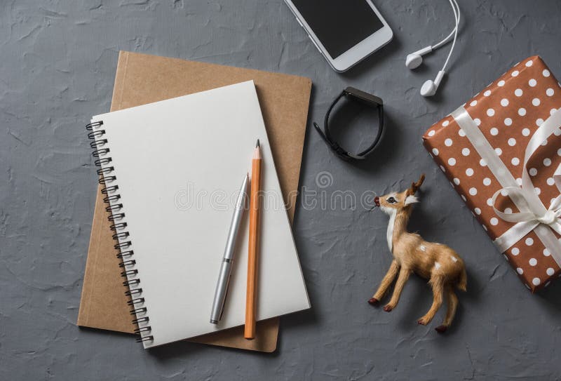 Empty blank notebook, gift box, christmas decoration reindeer, phone on office desk top view.