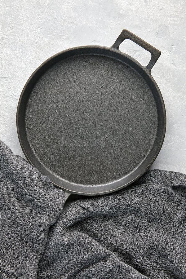 An Empty Cast Iron Skillet and a Gray Kitchen Napkin on a Gray Concrete