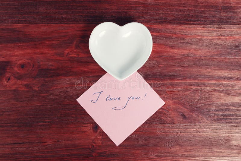 Empty ceramic saucer in the shape of a heart and a note `I love you` on a dark wooden table royalty free stock images Empty ceramic saucer in the shape of a heart and a note `I love you` on a dark wooden table royalty free stock images