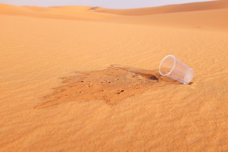 Empty glass of water on a desert land showing dehydration and water shortage concept