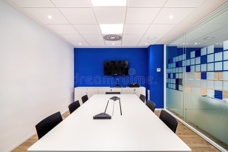 Empty meeting room for conversation with table, chairs, television in modern office interior with blue and white walls.