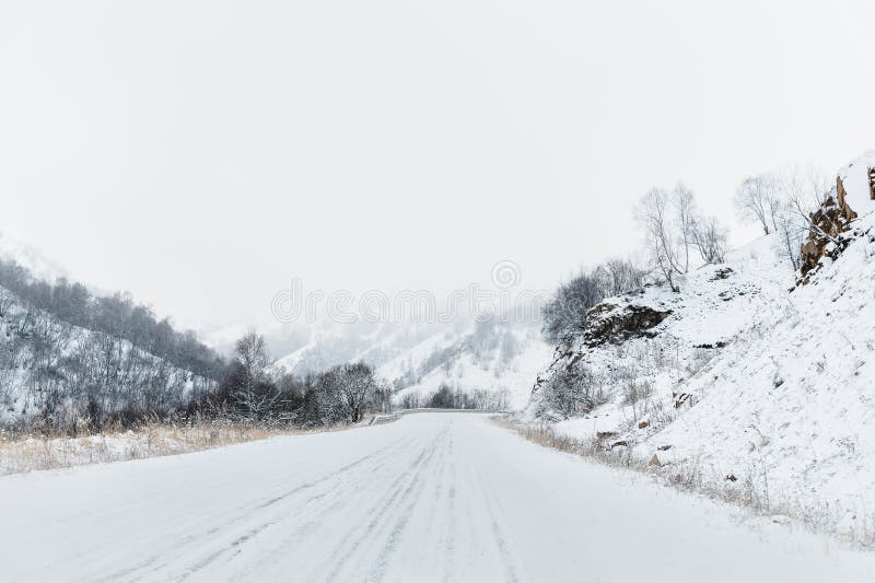 Empty mountain asphalt road in winter covered with snow on a cloudy day. The concept of driving a car in winter ice and