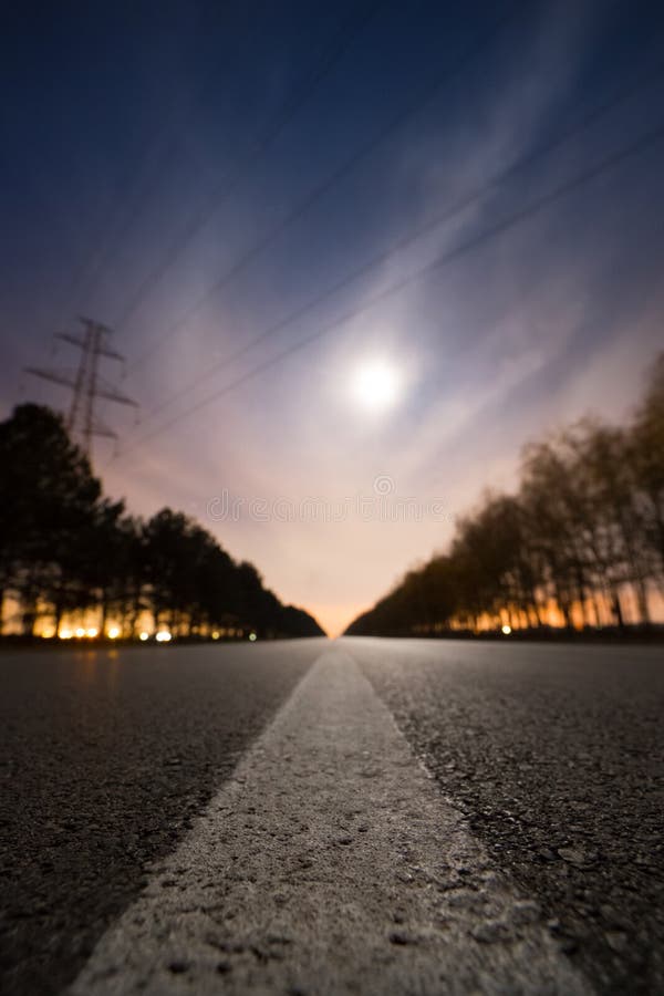 Empty night asphalt road, bright full moon behind clouds and city light behind two rows of trees on both side of road royalty free stock images Empty night asphalt road, bright full moon behind clouds and city light behind two rows of trees on both side of road royalty free stock images