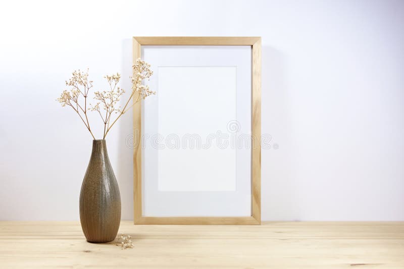 Machetă cu cadru gol și o vază ceramică brună cu tifilesofilă pe o masă din lemn, pe un perete gri deschis, minim stock photo