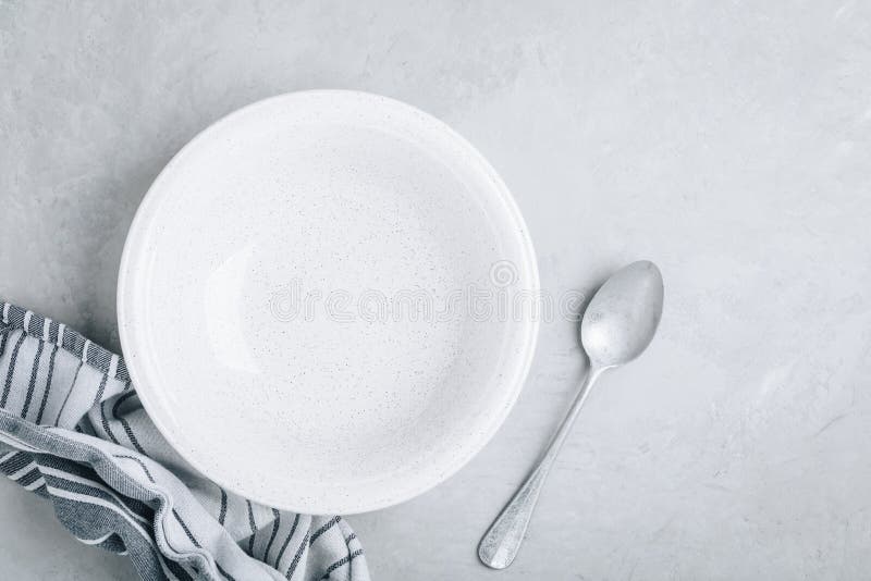 Empty plate or bowl with spoon and linen napkin on gray stone concrete background