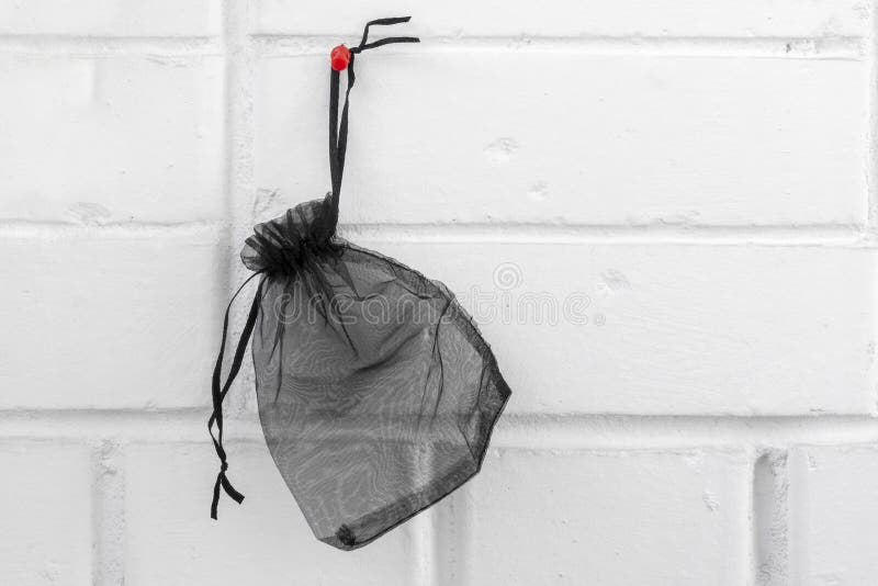 Empty Small Black Gift Bag Hanging on Red Pin Against White Brick Wall
