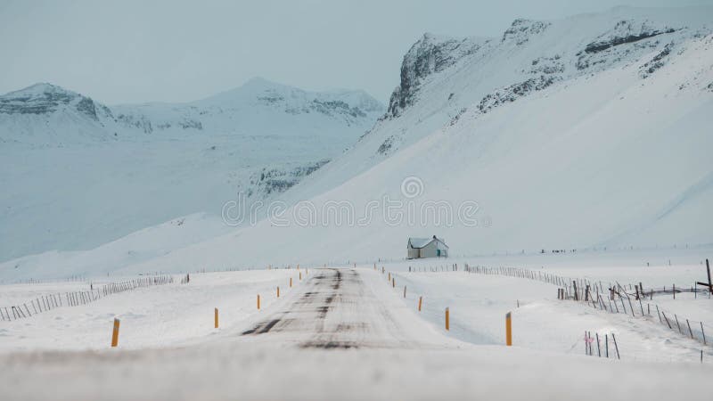 Empty snowy road and a small house in the end of it in a rocky area, Iceland