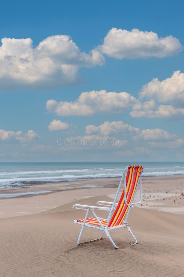 Empty Striped Beach Chair on Top of a Dune Facing the Sea. Vertical