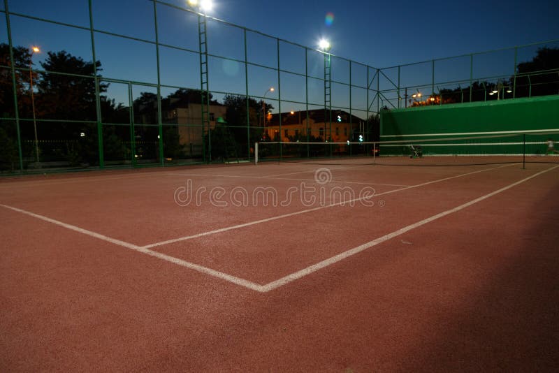 An empty tennis court at night, lit by bright lights