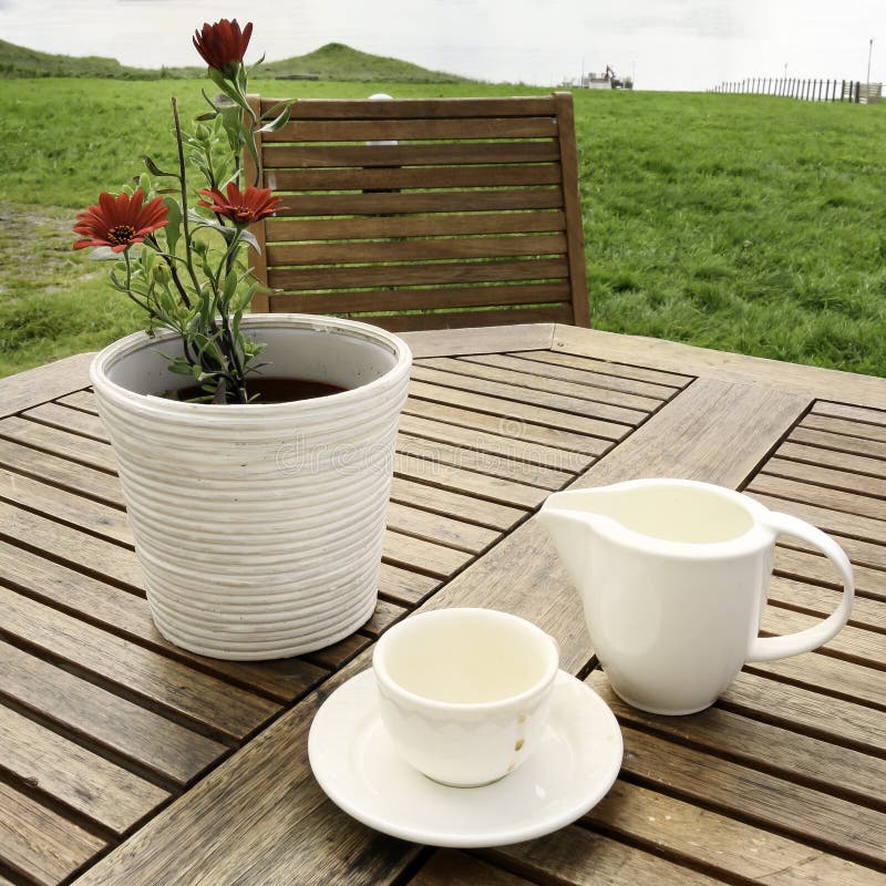 A coffee cup, a milk pitcher and a white flower pot on a table