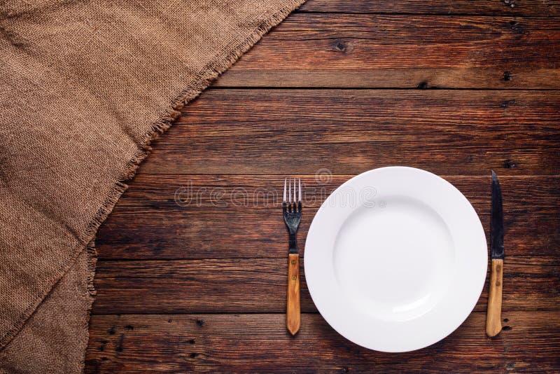 Empty white plate with old fork and knife on rustic wooden background. Vintage rustic recipe book background stock images, royalty-free photos and pictures