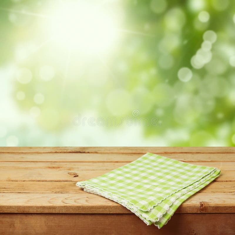 Empty wooden deck table with checked tablecloth over green nature bokeh background