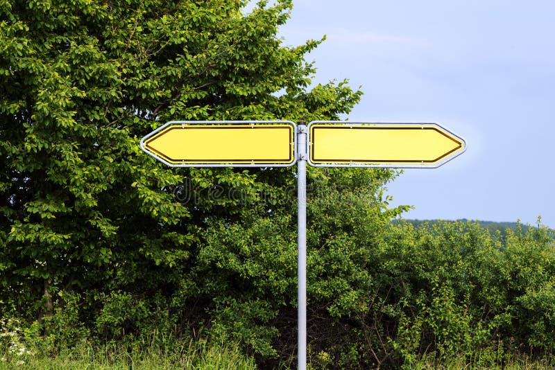 Empty yellow road signs pointing in opposite directions against stock photos