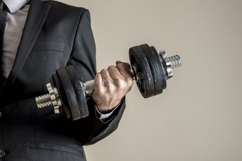 En affärsman i affärsdräkten som gör hantelbiceps, krullar royaltyfria bilder En affärsman i affärsdräkten som gör hantelbiceps, krullar royaltyfria bilder