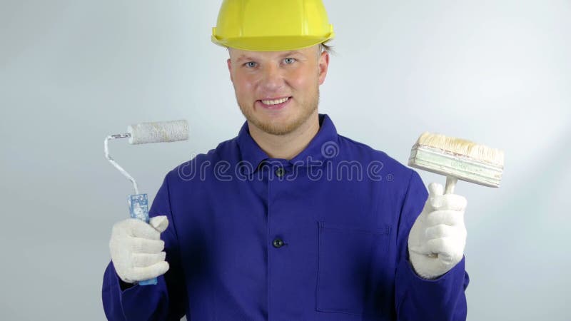 En arbetare med en färgvält i händerna för att måla på en vit bakgrund i en hjälmporträtt av en byggare som leker