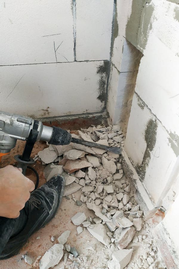En arbetare med en hålapparat bryter väggen och fundamentet av huset för att föra elektriska trådar arkivbilder En arbetare med en hålapparat bryter väggen och fundamentet av huset för att föra elektriska trådar arkivbilder