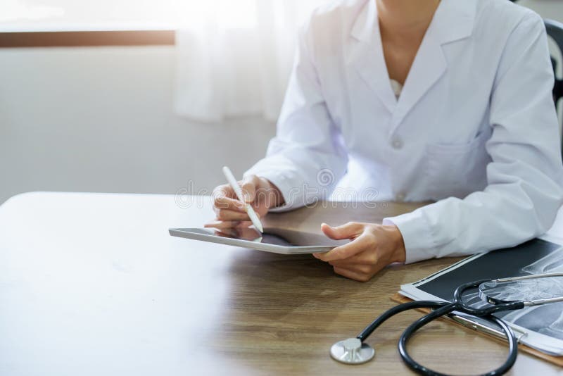 En asiatisk kvinnlig läkare använder en tablettdator för att analysera patientsymptom före behandling.