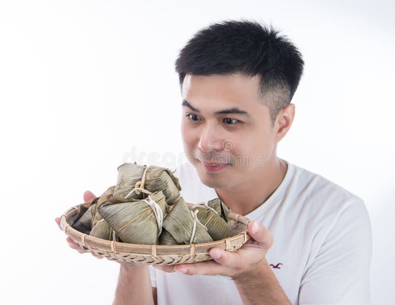 En Asien man ser Zongzi eller risklimpen med den roliga framsidan och leende och känner sig intresserade i dem på Dragon Boat Fes arkivfoto En Asien man ser Zongzi eller risklimpen med den roliga framsidan och leende och känner sig intresserade i dem på Dragon Boat Fes arkivfoto