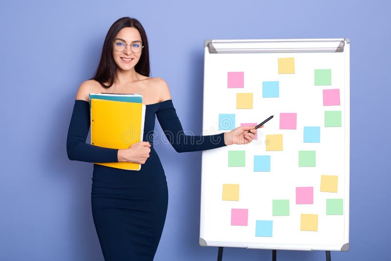 En attraktiv leende kaukasisk kvinna som sitter bredvid whiteboard med flerfärgade klisterlappar, flicka med blå axlar arkivfoton En attraktiv leende kaukasisk kvinna som sitter bredvid whiteboard med flerfärgade klisterlappar, flicka med blå axlar arkivfoton