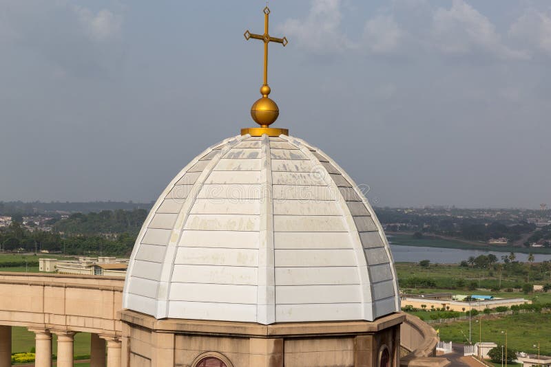 The Basilica of Our Lady of Peace Basilique Notre Dame de la Paix is situated in Yamoussoukro, Ivory Coast Cote d`Ivoire in West Africa. It is the largest church in the world. This is a view of one of the minor domes over the colonnades. There is a cross over the dome. A lake is seen in the distance. The Basilica of Our Lady of Peace Basilique Notre Dame de la Paix is situated in Yamoussoukro, Ivory Coast Cote d`Ivoire in West Africa. It is the largest church in the world. This is a view of one of the minor domes over the colonnades. There is a cross over the dome. A lake is seen in the distance.