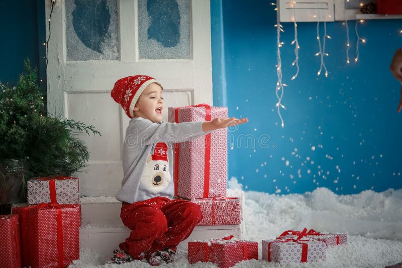 En babypojke på juldagsdagen sitter på golvet nära presentboxar och tar upp händerna som om han skulle fånga snöflingor arkivfoton