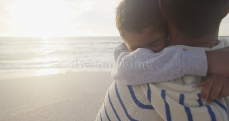 En bild av den hispaniske fadern som tar hand om sonen på stranden vid solnedgången