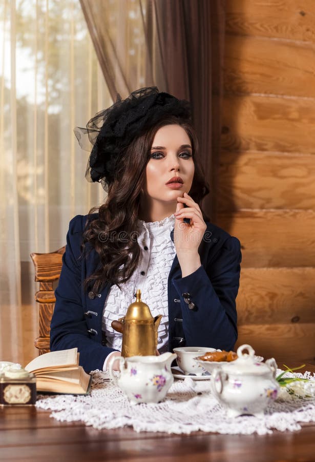 En bild av en drömmande caucasian brunette-kvinna som klär sig i retro-klänning med kaffepott och sylt vid bordet inomhus arkivfoton