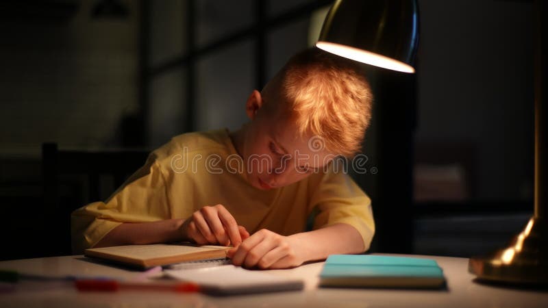 En bild av smart koncentrerad skolpojke som snabbt läser en pappersbok som kör ett finger längs en sida av boken som sitter vid bo