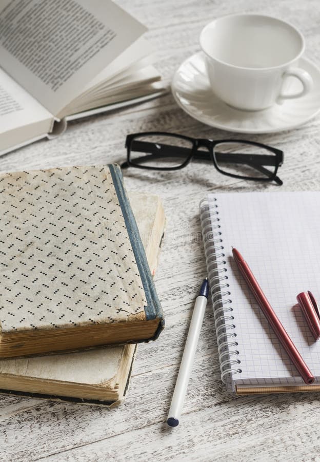 En bunt av böcker, anteckningsboken och exponeringsglas, kaffekopp på den vita trätabellen fotografering för bildbyråer En bunt av böcker, anteckningsboken och exponeringsglas, kaffekopp på den vita trätabellen fotografering för bildbyråer