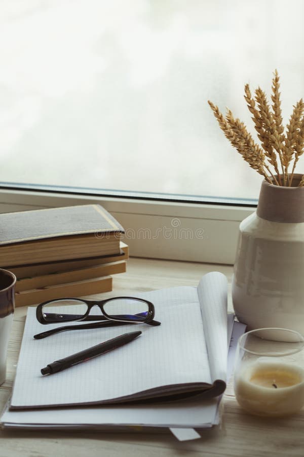 En bunt av böcker, koppen kaffe, buketten av kärnor, exponeringsglas, anteckningsboken och pennan över ett fönster fotografering för bildbyråer En bunt av böcker, koppen kaffe, buketten av kärnor, exponeringsglas, anteckningsboken och pennan över ett fönster fotografering för bildbyråer