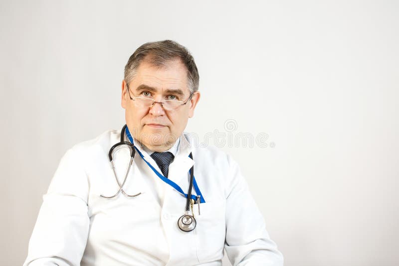 En doktor i ett vitt lag och band ser framåtriktat, har en whist en stetoskop och ett emblem på hans hals, och det finns pennor i arkivfoton En doktor i ett vitt lag och band ser framåtriktat, har en whist en stetoskop och ett emblem på hans hals, och det finns pennor i arkivfoton