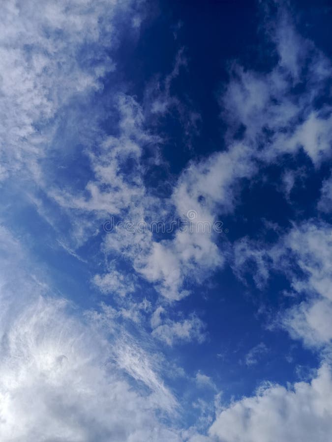 En dynamisk blå himmel med varierade vita molnformationer som är lite klokare och andra som gör att en texturerad vertikal sammans arkivbilder