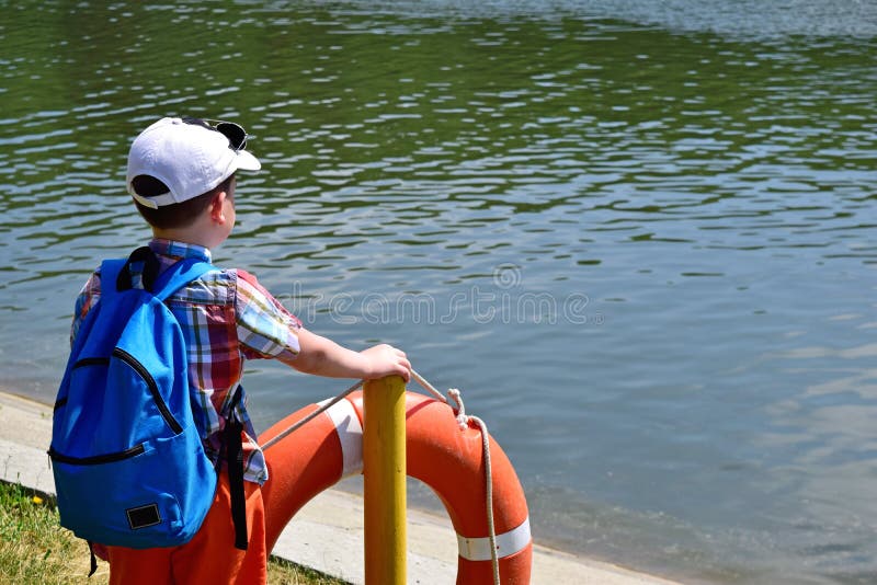 En el banco del río es un muchacho y mira el agua foto de archivo En el banco del río es un muchacho y mira el agua foto de archivo