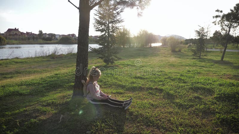 En el bosque, Joven en el parque mirando el telÃ©fono mÃ³vil. Chica sentada junto al Ã¡rbol con telÃ©fono. Concepto de gadget