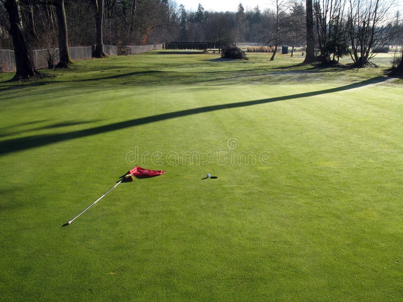 Golf ball beside hole with flag laying on ground. Golf ball beside hole with flag laying on ground.